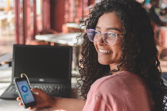 A young milennial woman smiling with her phone  open to a trading app. 