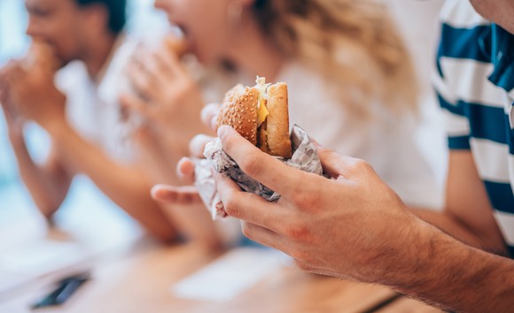 Closeup on hands holding a burger wrapped in foil.