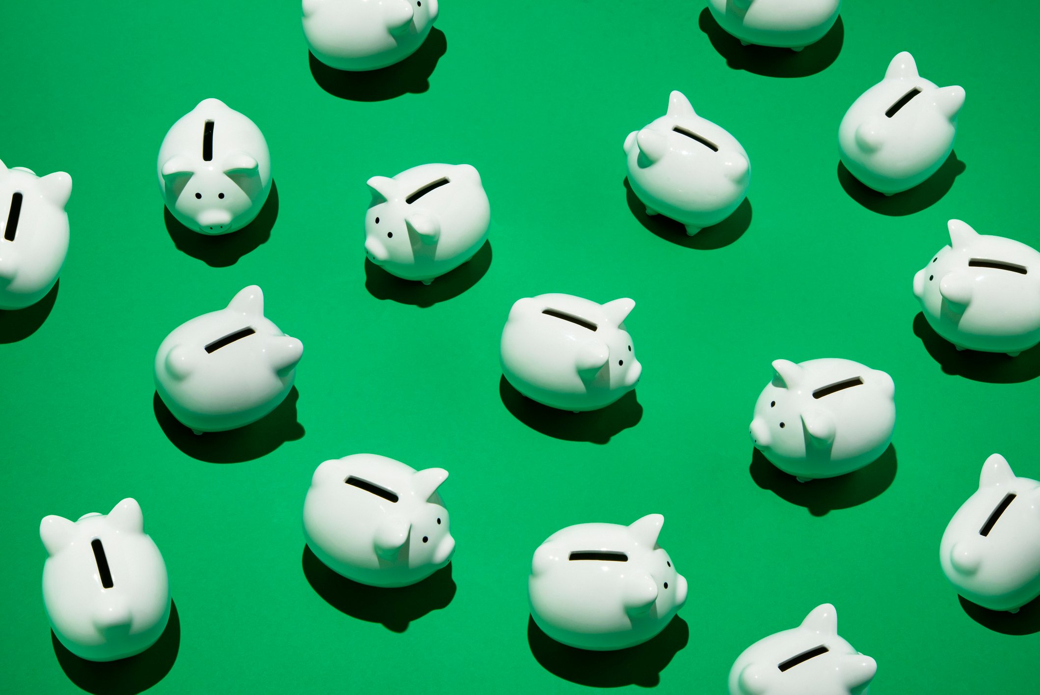 A group of small white piggy banks against a green background.