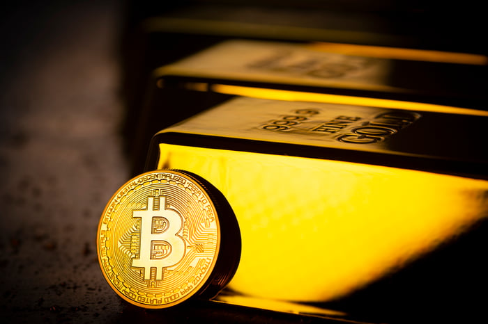 A coin bearing the Bitcoin symbol rests against one of many gold bullion bars.