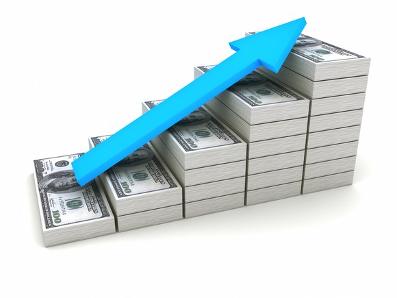 A stack of dollar bills with a blue arrow laying on top of it.