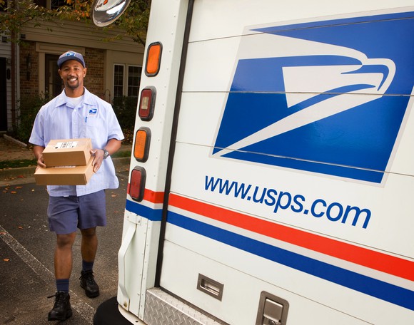 Postal carrier carrying packages next to a USPS truck.