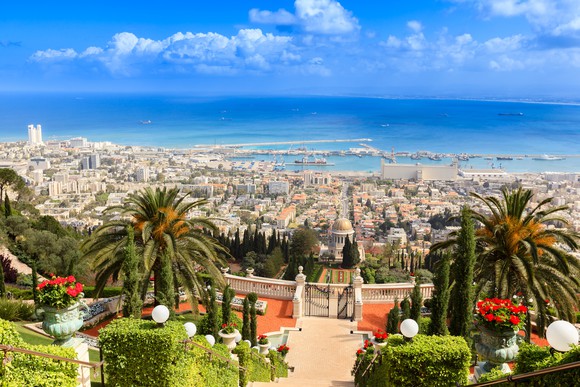 The port city of Haifa in Israel, with palms in the foreground and the Mediterranean in the background.