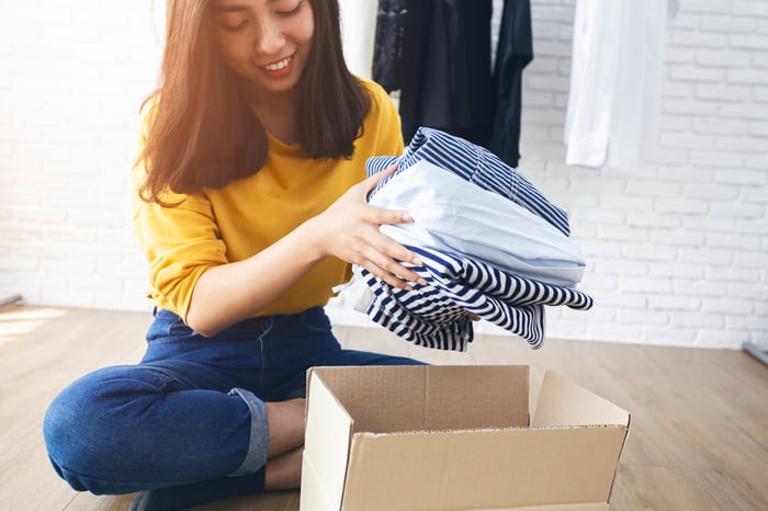 A smiling young woman removes clothes from a box.