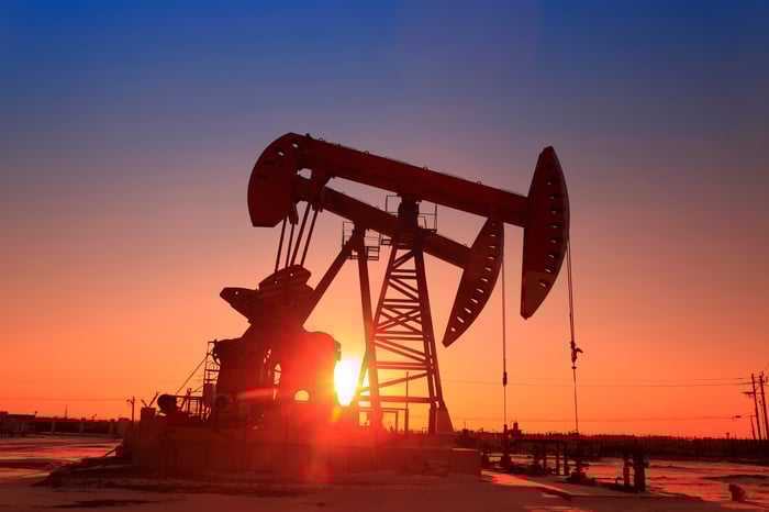 The sun setting behind an oil pump.
