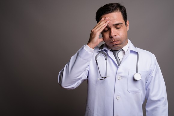 Doctor looking stressed with a hand on his forehead. 