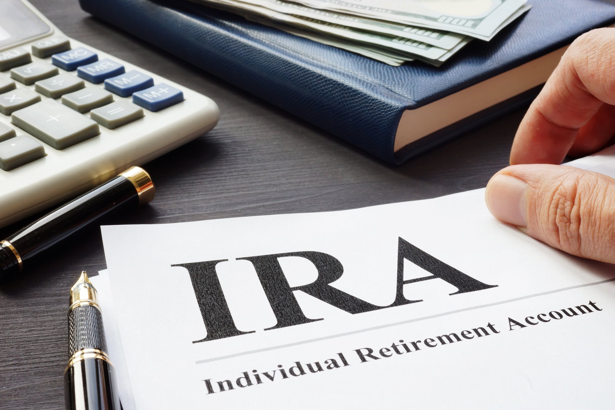 Document that says IRA on surface next to calculator, pen, and book with bills on it