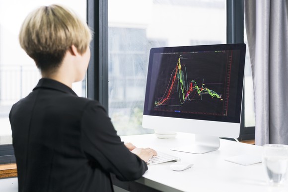 A woman looks at a stock chart that has a high peak and comes back down.