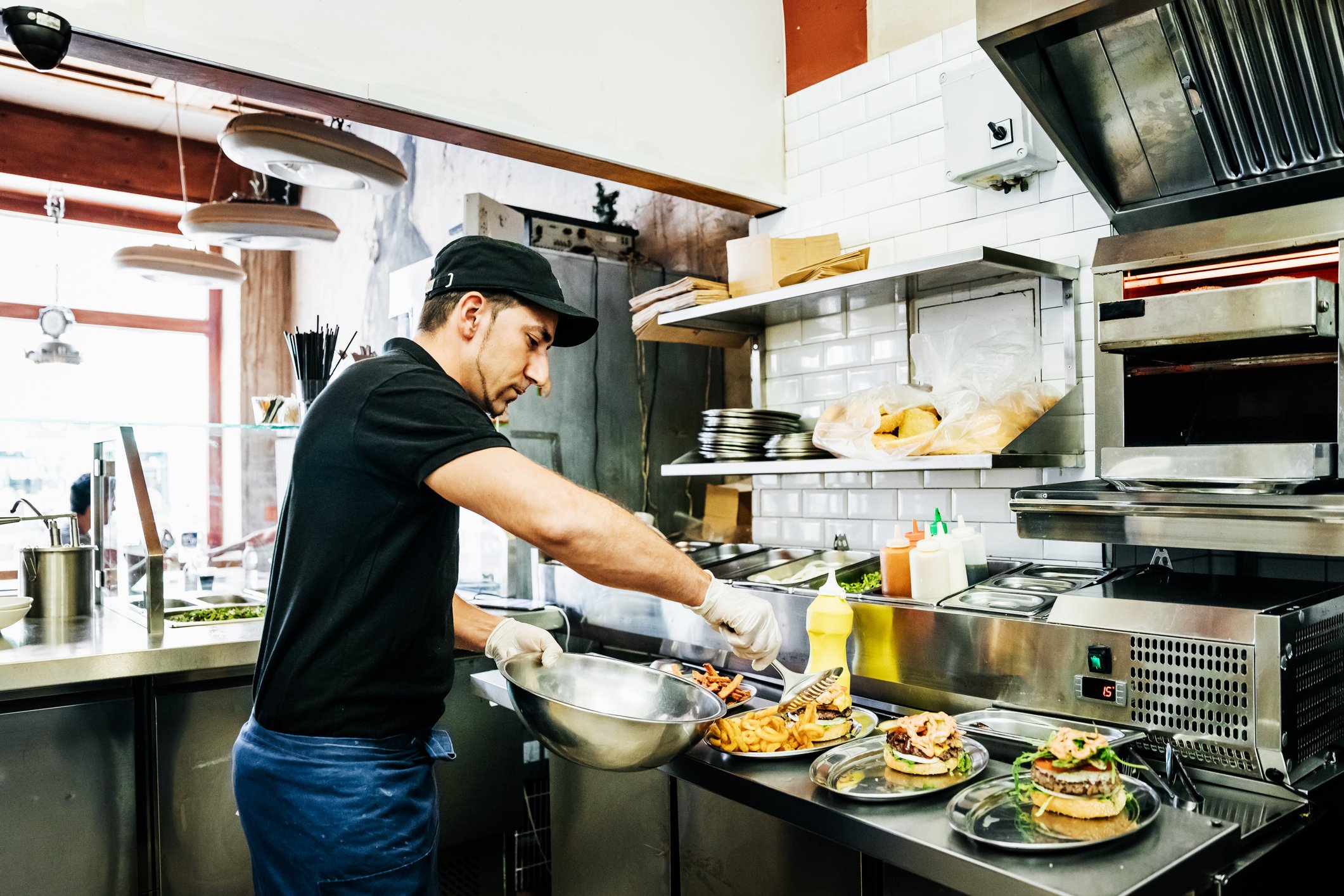 A restaurant worker in the kitchen putting food on a plate.