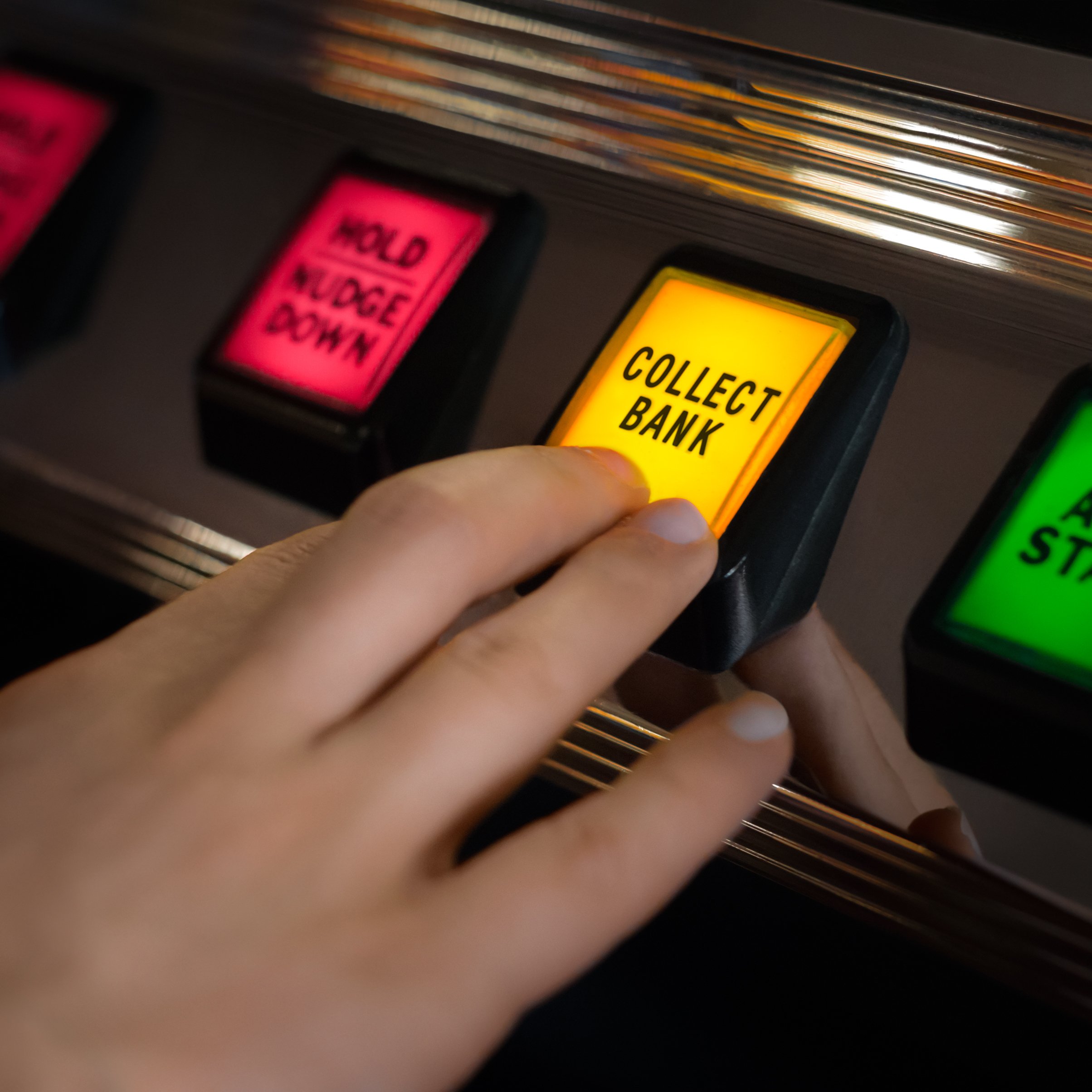 A hand pushes a yellow button on a casino machine, marked Collect Bank.