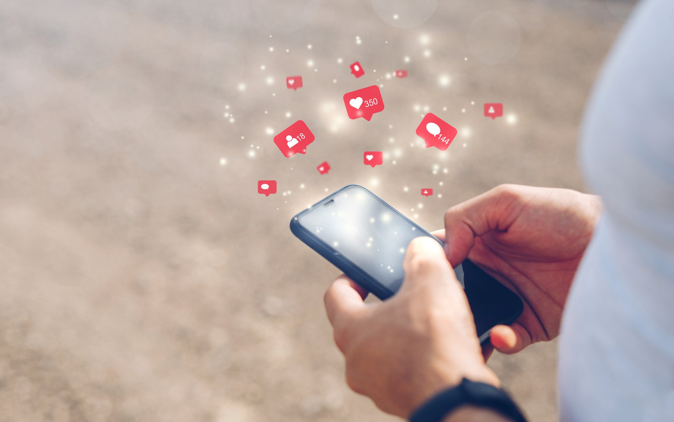Closeup of hands on a phone with heart emojis popping out.