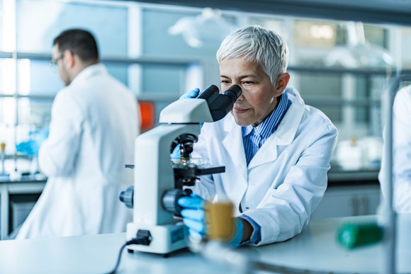 A scientist in a lab setting looks into a microscope.