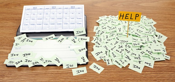 Pile of IOU notes with HELP sign on top, next to checkbook with IOU notes on it.