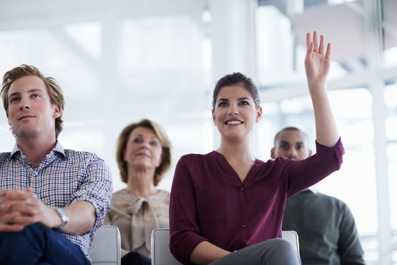 Woman sitting in classroom with her hand raised 