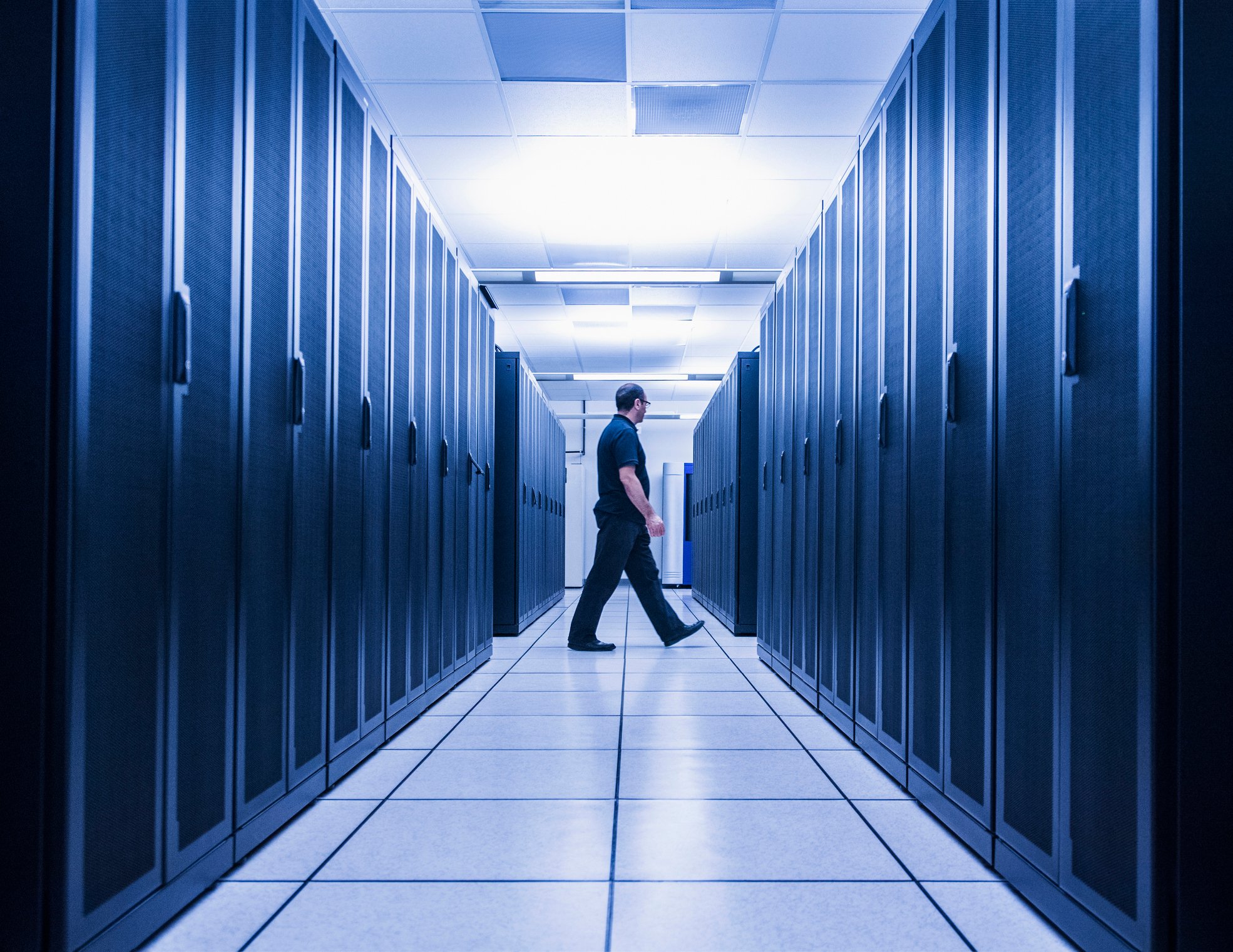 A man at the end of an aisle of servers in a server room