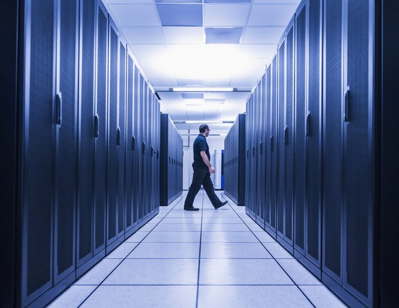 A man at the end of an aisle of servers in a server room