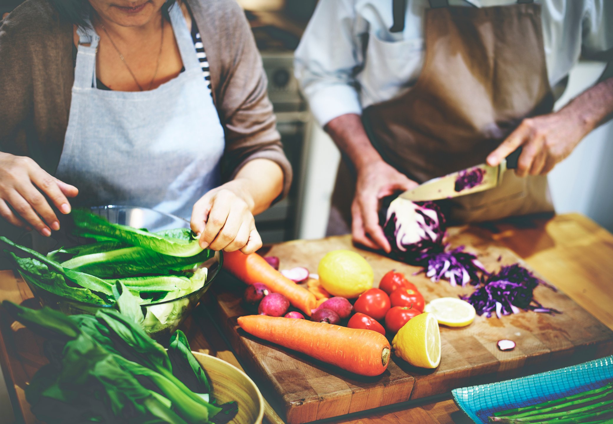 Two people chopping vegetables on a wooden cutting board