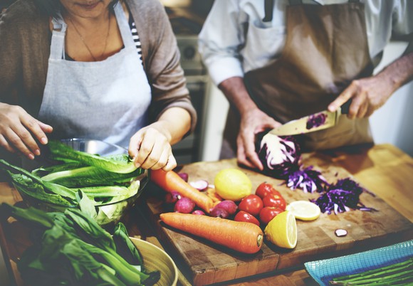 Two people chopping vegetables on a wooden cutting board