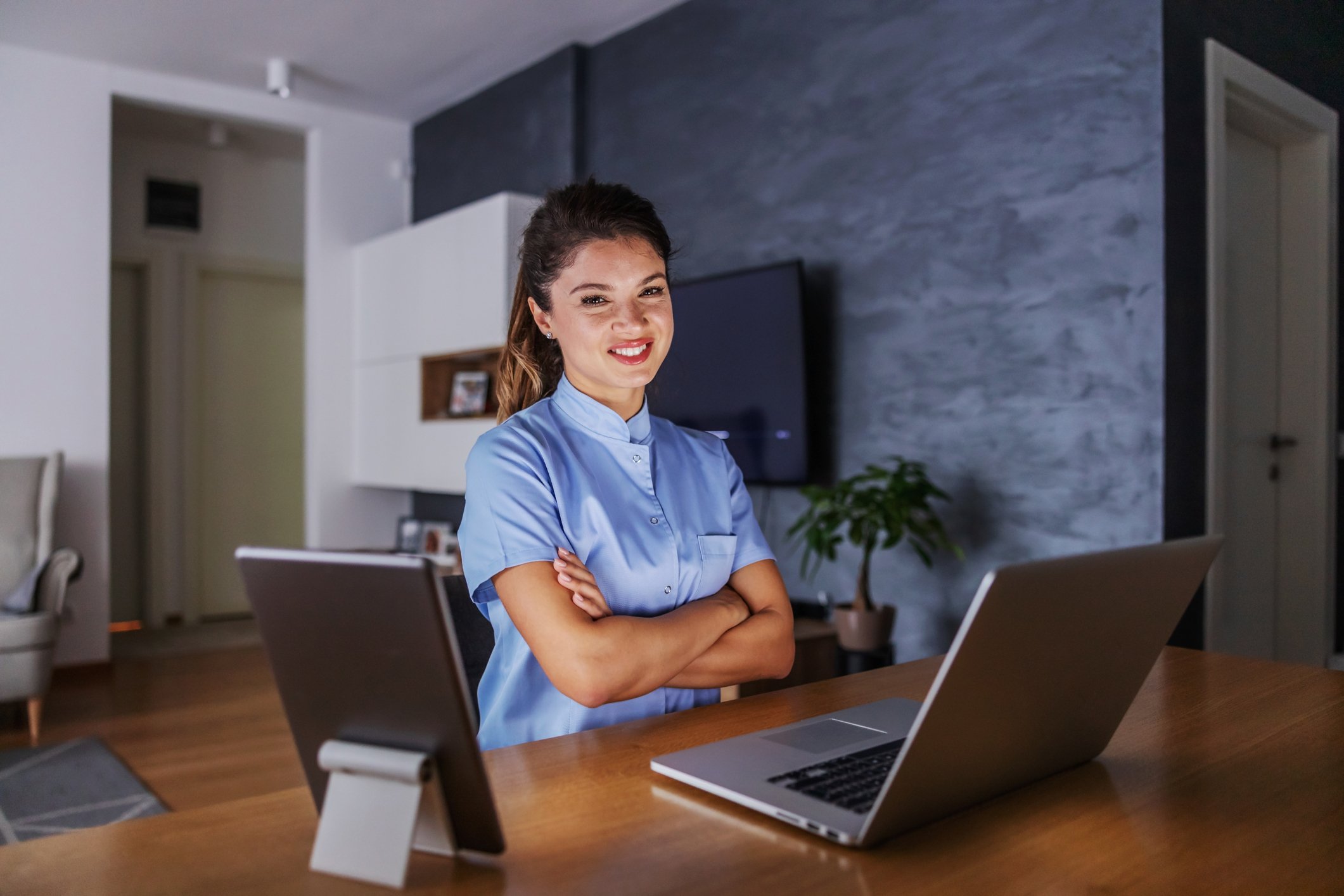 Smiling young woman with her arms folded while sitting in front of a laptop
