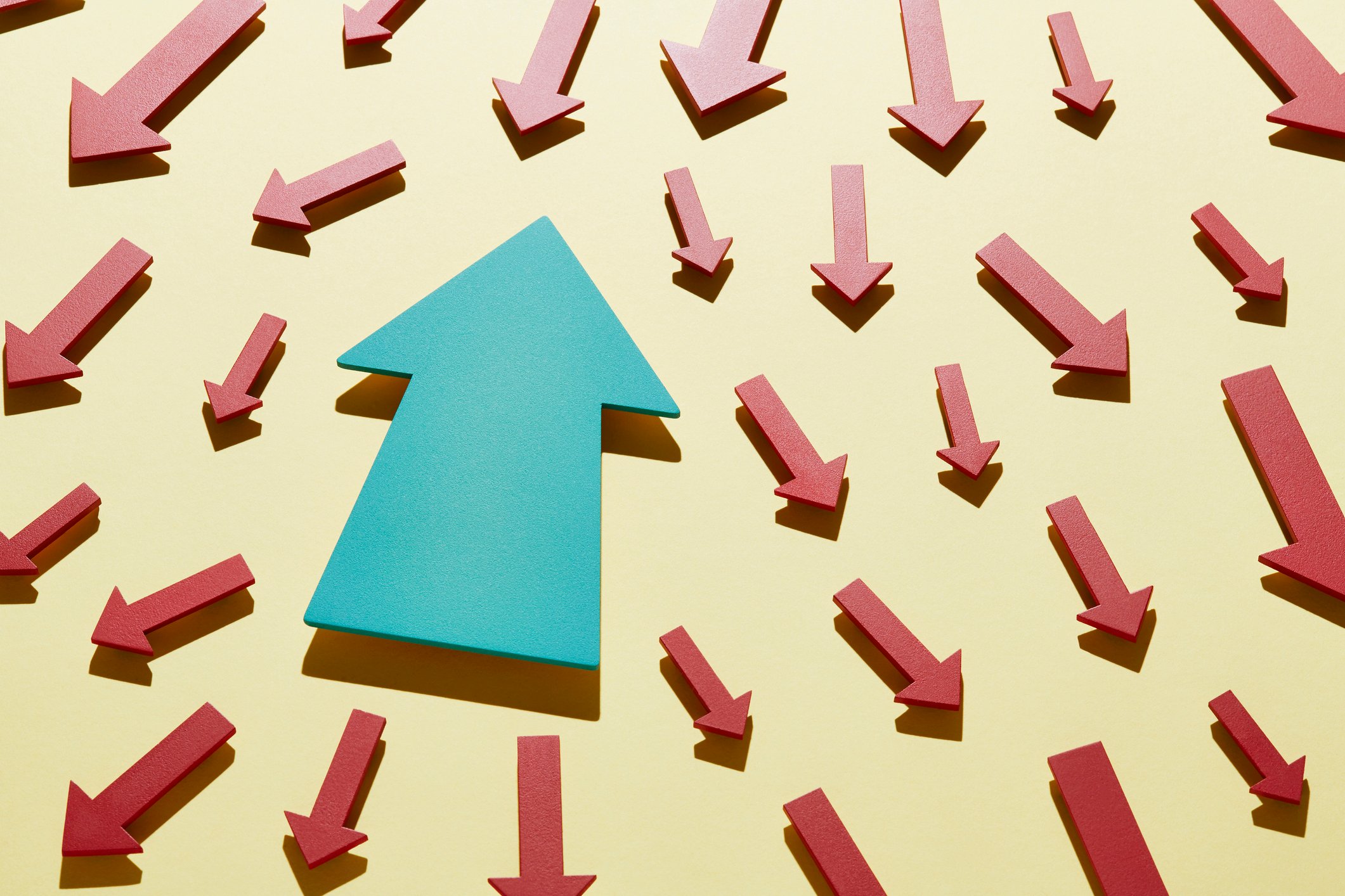 Blue arrow pointing up against many red arrows pointing down