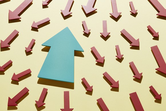 Blue arrow pointing up against many red arrows pointing down