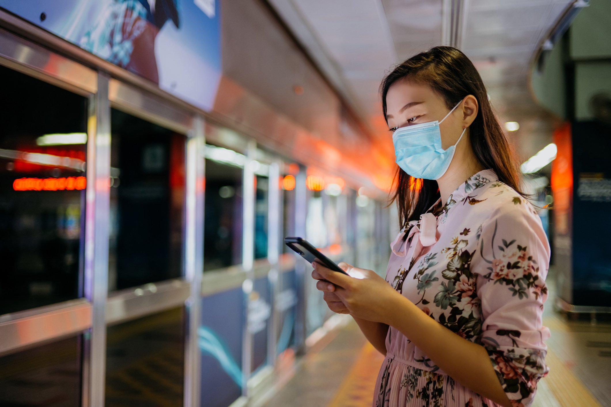 Young woman wearing a mask while using a smartphone in a public area.