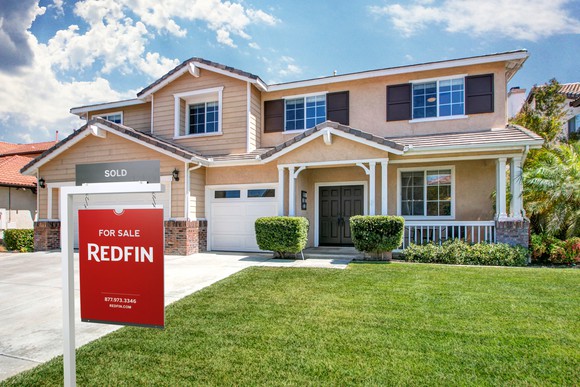 A Redfin sales listing sign in front of a two-story home. 