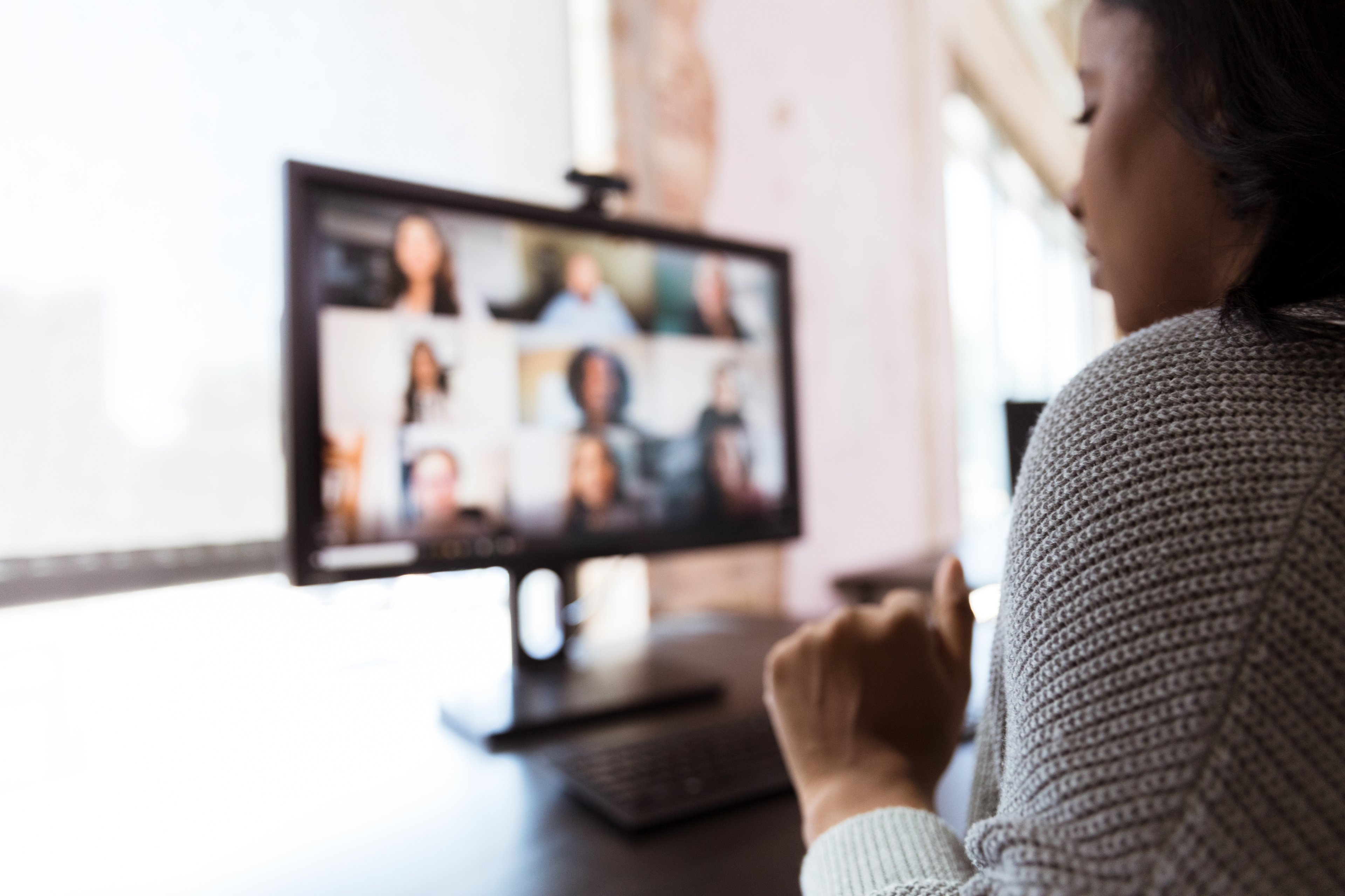 A woman views a screen showing several coworkers teleconferencing.