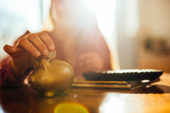 A woman puts coins in a golden piggy bank. The camera focused tightly on the foreground, blurring the woman.