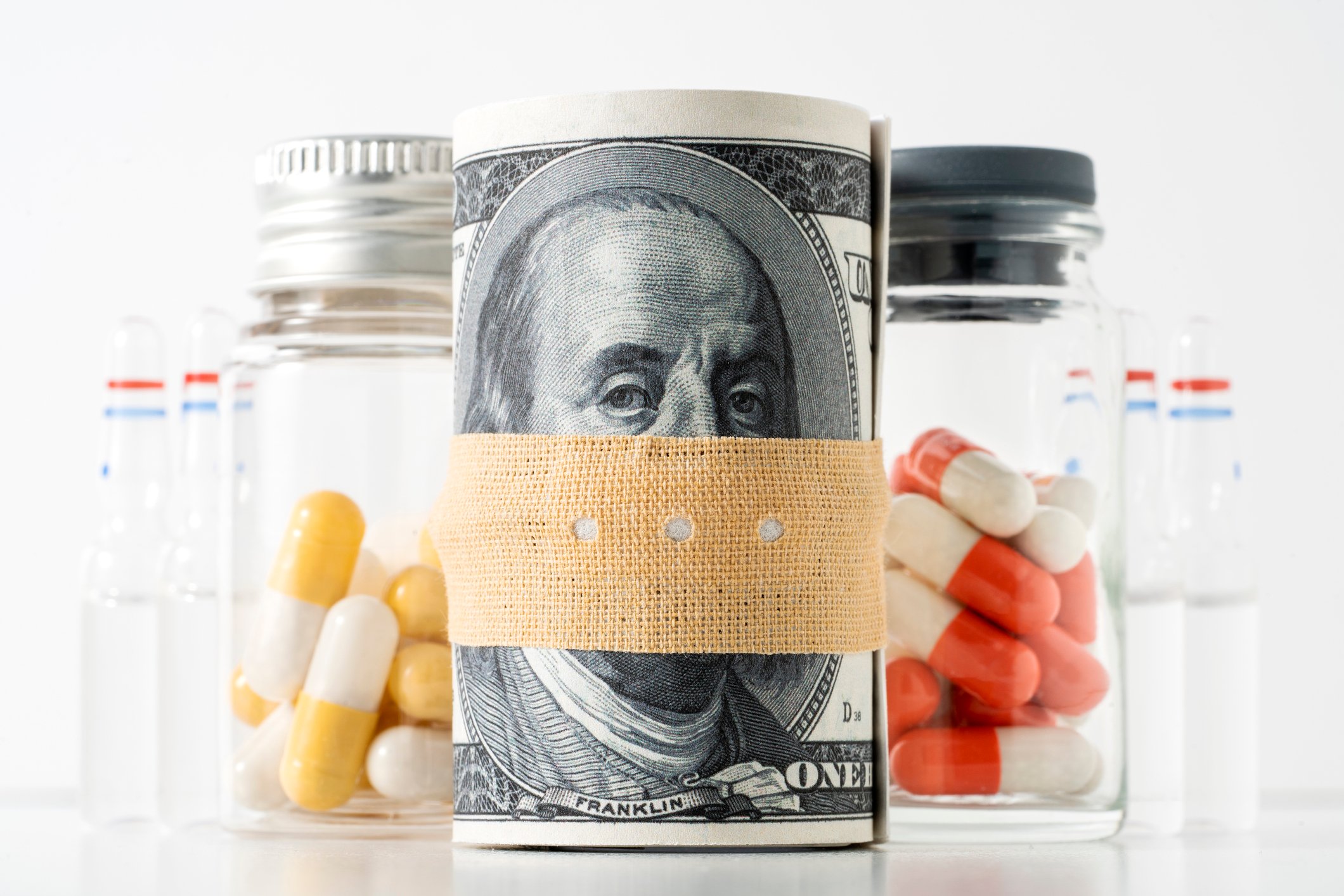 A rolled-up dollar bill wrapped in a bandage alongside some pill bottles.