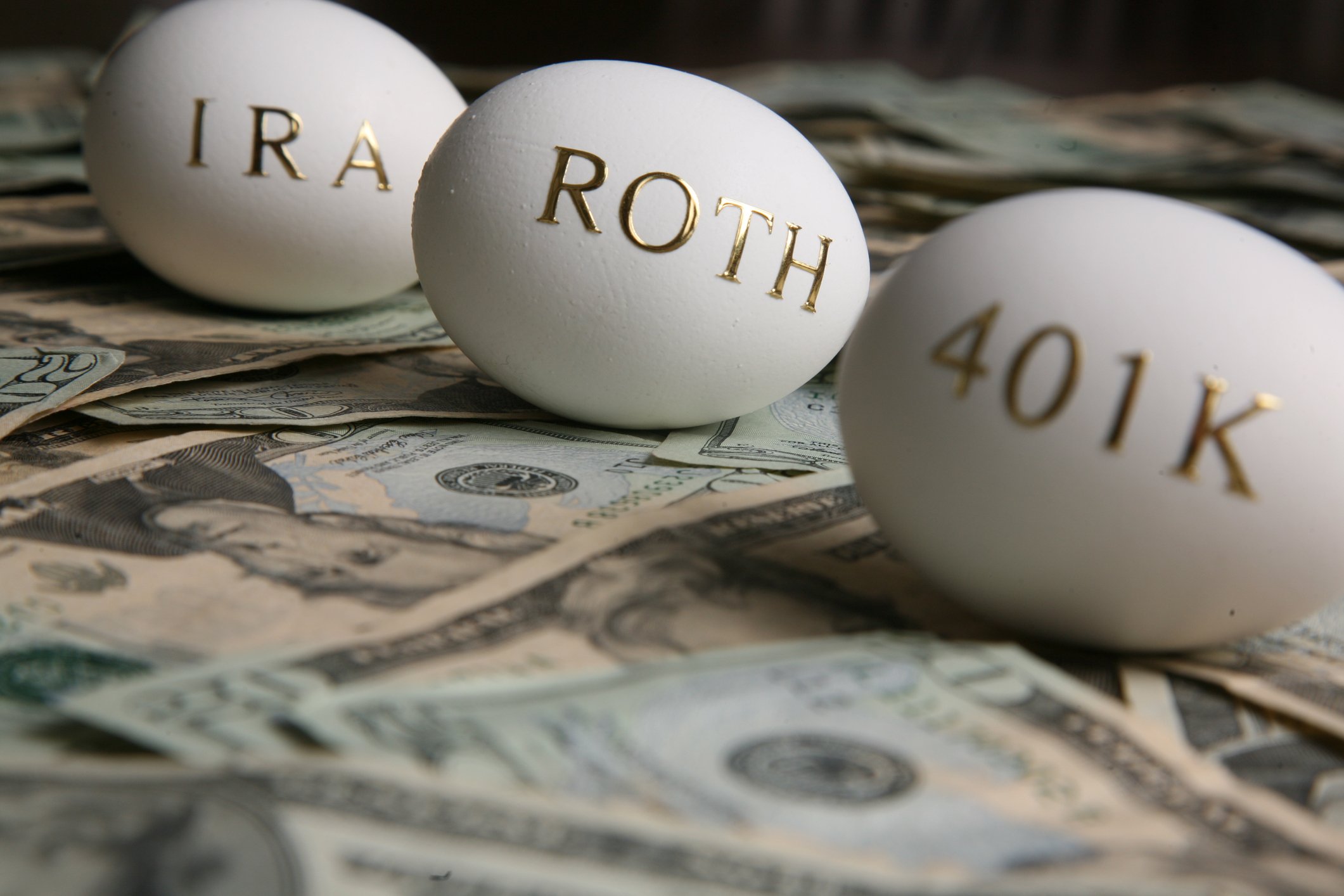 Eggs with "IRA", "Roth", and "401k" written on them, sitting on bed of money.
