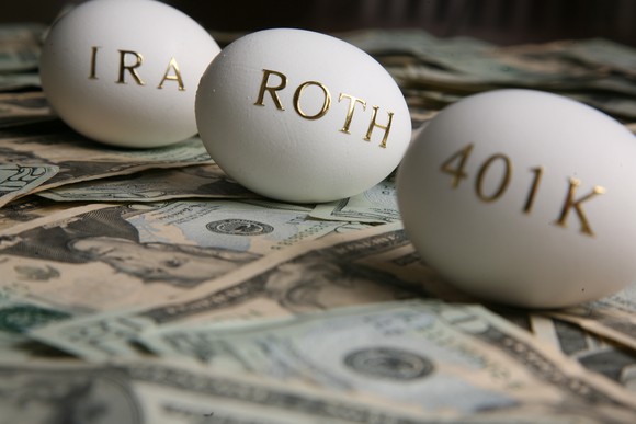 Eggs with "IRA", "Roth", and "401k" written on them, sitting on bed of money.