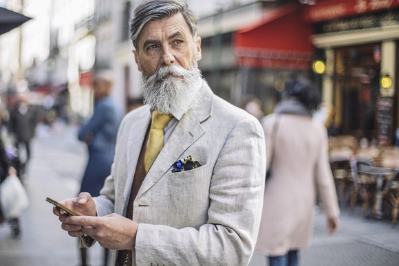 A bearded man texting in the street.