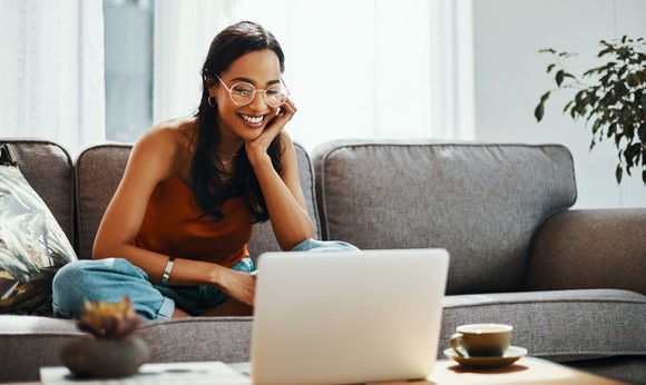 Girl relaxing on sofa and smiling at laptop