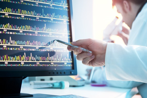 A researcher gestures to a readout of a DNA sequence.