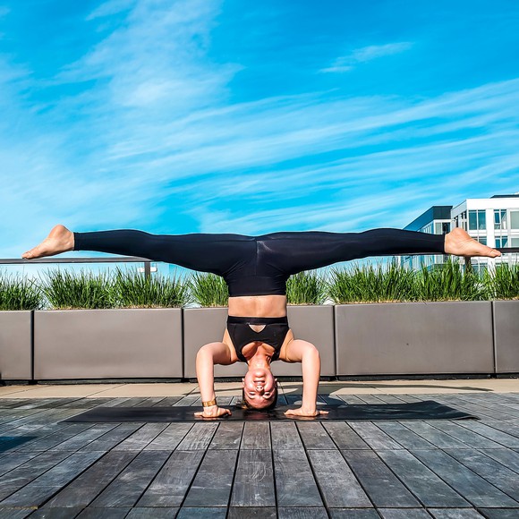 A woman does yoga on her deck in front of a blue sky.
