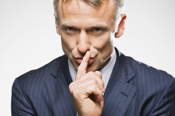 A man in a suit has his finger in front of his mouth, shushing others