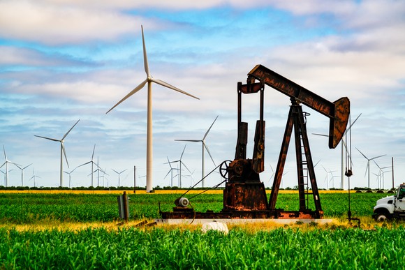 An oil pumpjack in a field with wind turbines.