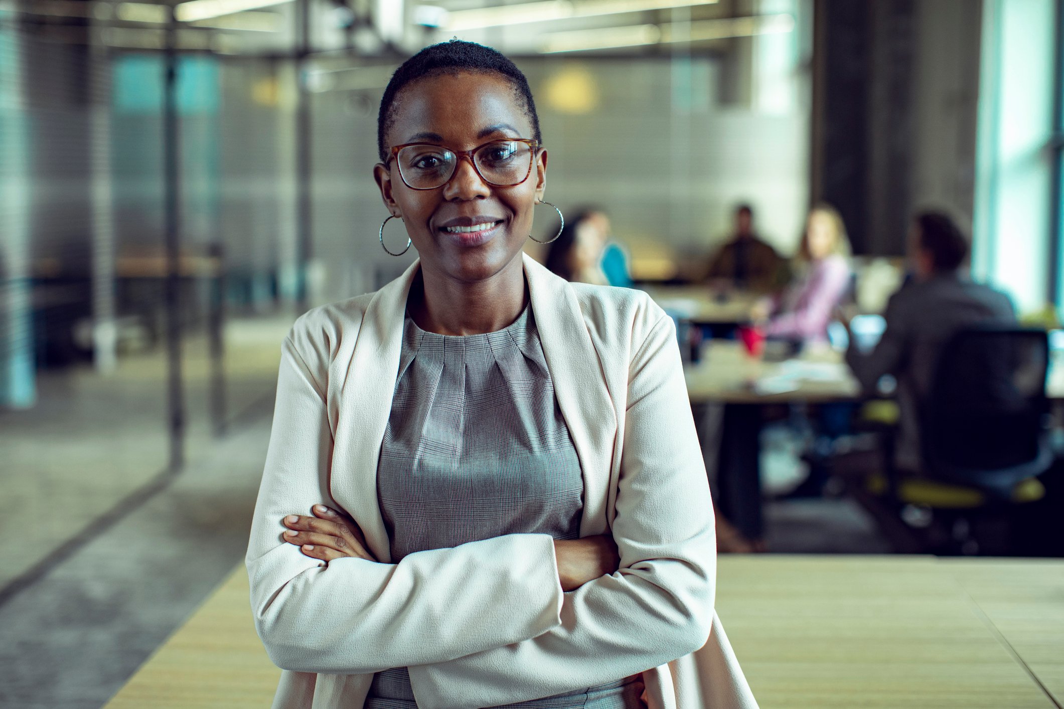 Smiling woman with arms crossed, standing in corporate meeting room
