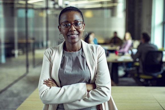 Smiling woman with arms crossed, standing in corporate meeting room