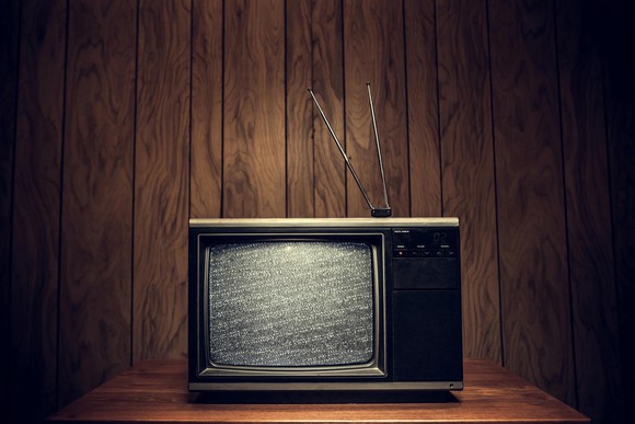 Old-style television with static and antenna on wood shelf with wood paneling behind.