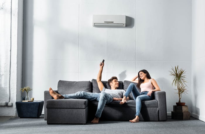 Two people sitting on a sofa beneath an air conditioner 