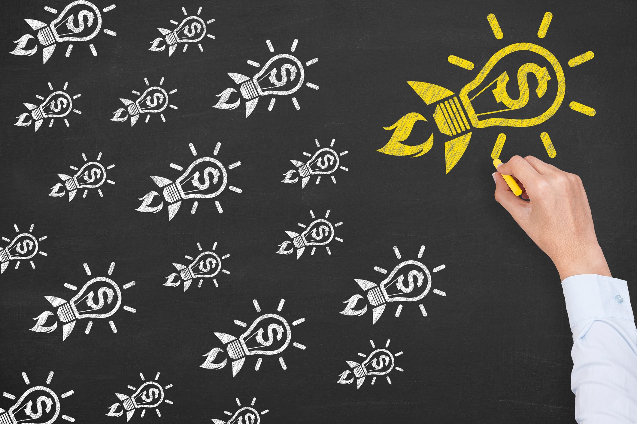 Chalkboard drawing of rockets shaped like lightbulbs with dollar signs in them with one colored yellow and larger than the others