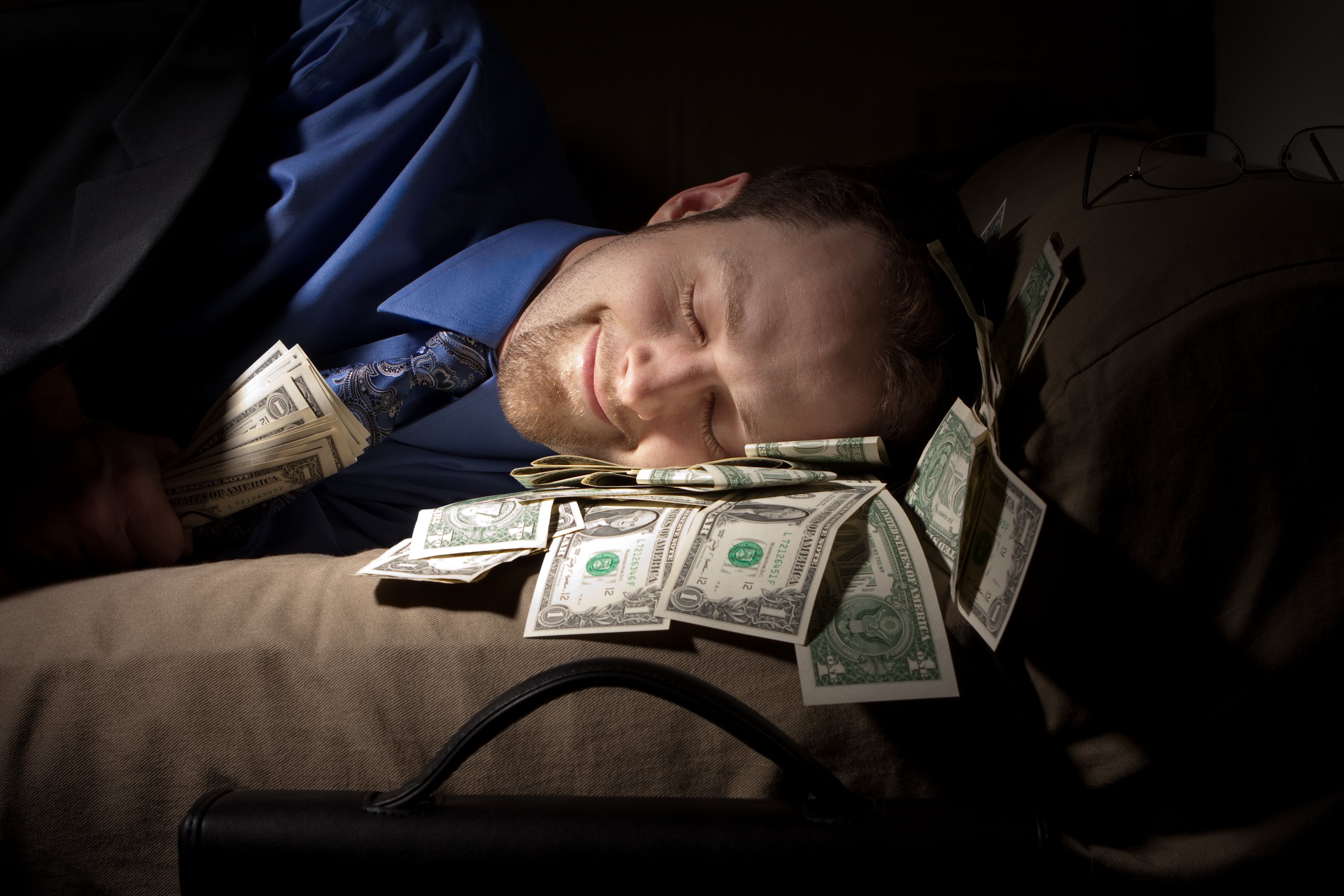 A man sleeps on a pile of dollar bills.