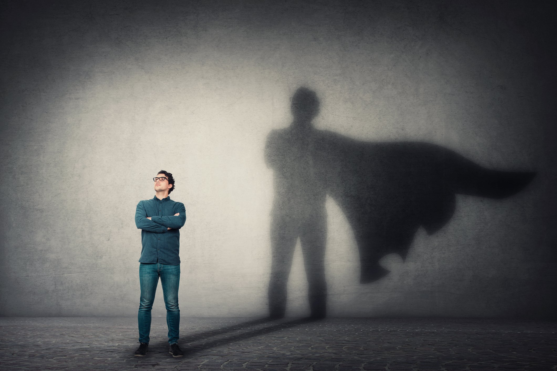 A man crosses his arms and casts the shadow of a superhero in a cape.