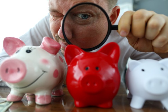 A man examines piggy banks with a magnifying glass.