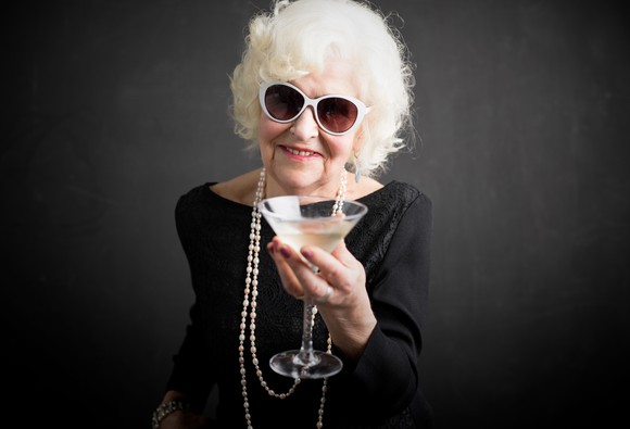 A senior woman in sunglasses enjoys a martini.