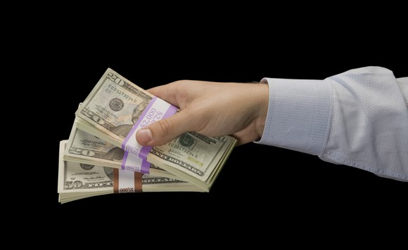 A man holding out three stacks of $20 bills.