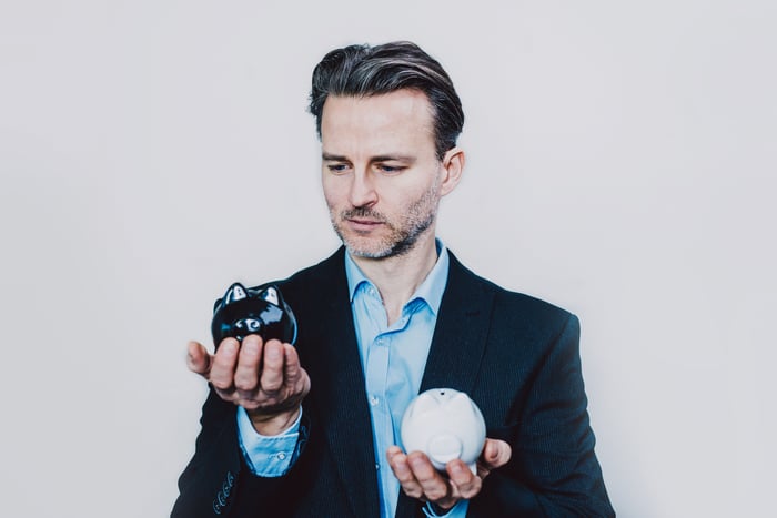 A man  in business casual attire weighs two balls in each one of his hands. 