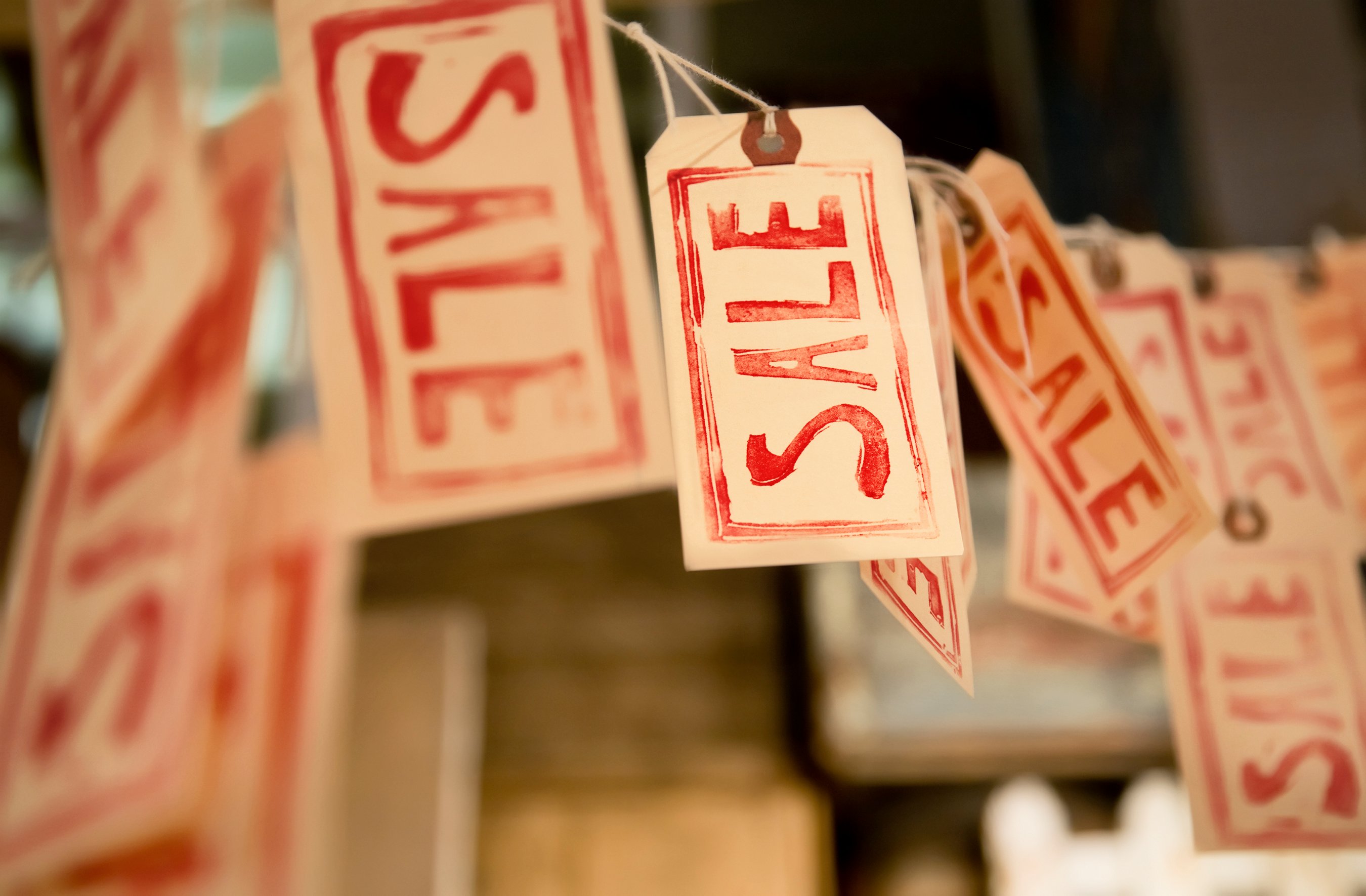 Paper tags hanging from a string with the word sale written on them in red letters.